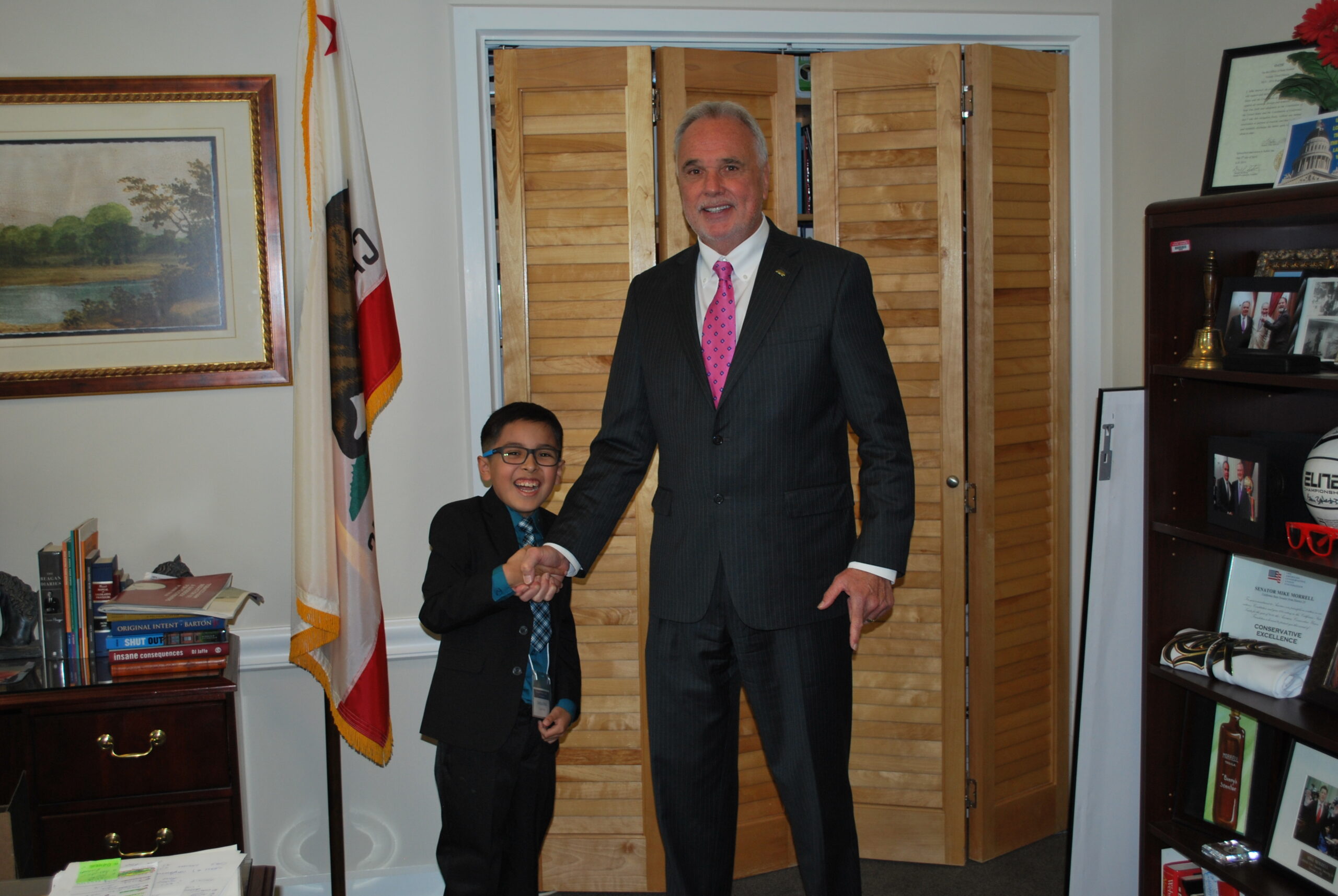 a young boy shaking hands with a legislator in his office at the California State Capitol
