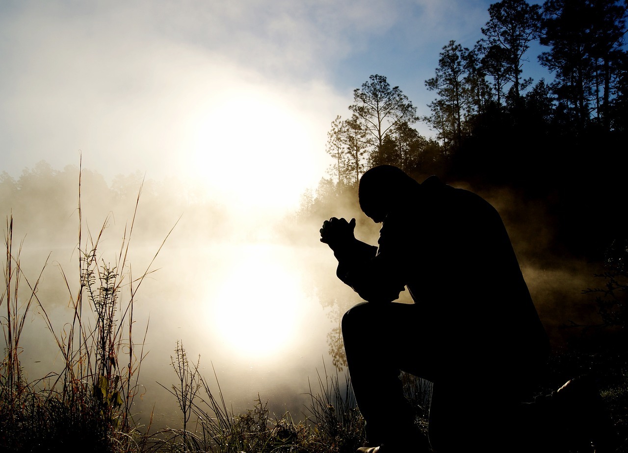 silhouette of man on one knee with his elbows on his right knee on a early foggy morning at a lake or a pond.
