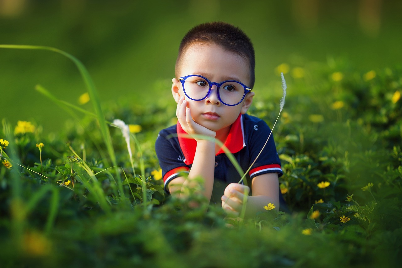 a child lying in grass with blue glasses